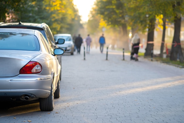 Cars parked in a row on a city street side on bright autumn day with blurred people walking on pedestrian zone.