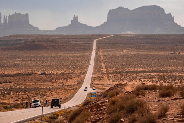 Cars on road amidst landscape leading towards monument valley during summer