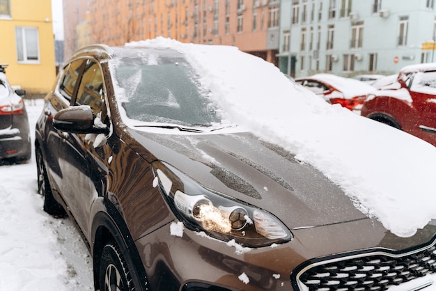 降雪後の雪の中の車。雪の降る冬、たくさんの雪。車の屋根、窓、ボンネットには雪が降っています。雪に覆われた駐車場の車。寒い雪の降る冬の天気