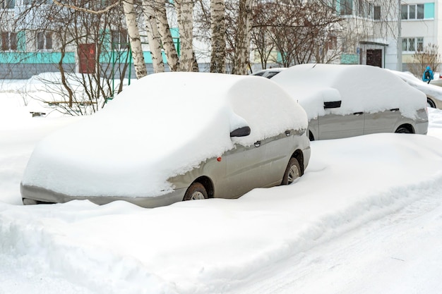 Auto sotto la neve in un parcheggio vicino a un condominio