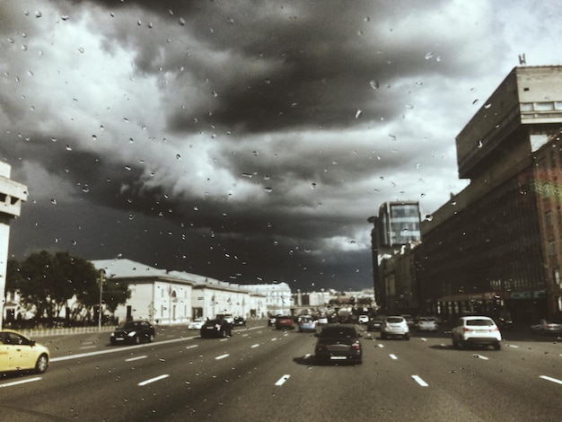 Photo cars on street seen through wet window against cloudy sky