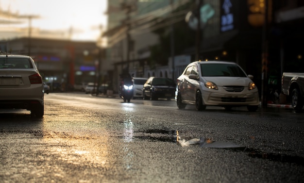 Auto su strada bagnata dopo la pioggia caduta con luce della sera in città, messa a fuoco selettiva. stagione delle piogge, sfondo del trasporto.