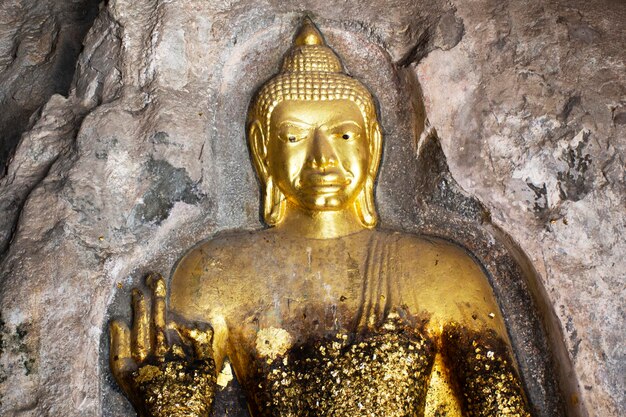 Carving steen en sculptuur boeddha beeld standbeeld op grotwand van Tham Khao Ngu voor thaise mensen reizen bezoek en respect biddende zegen mystiek in kalksteen bergrotspark in Ratchaburi, Thailand