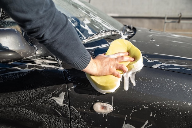 Carwash concept man was auto met zeep en gele spons