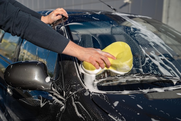 Концепция автомойки человек моет машину с мылом и желтой губкой