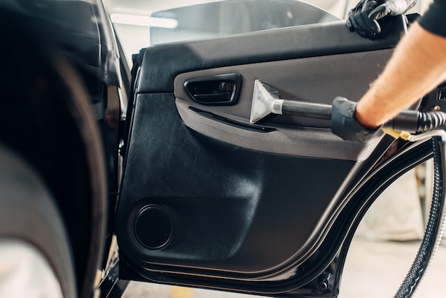 Foto servizio di autolavaggio, lavoratore di sesso maschile in guanti che rimuovono polvere e sporco dal rivestimento della porta.