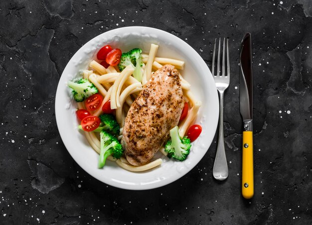 Casarecce pasta with broccoli cherry tomatoes and baked chicken breast on a dark background top view