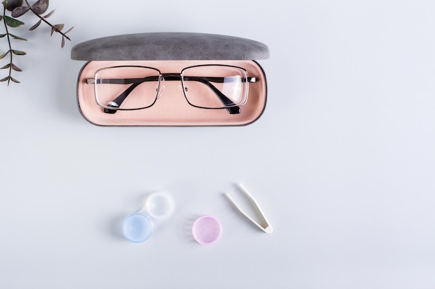 A case with glasses an open container with contact lenses and tweezers Top view