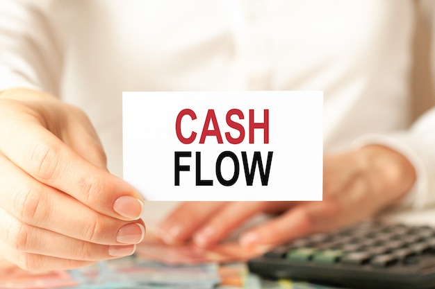 Cash flow is written on a white business card. a woman's hand holds a white paper card, white background. Business and advertising concept. Defocus.