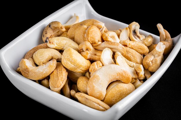 Cashew nuts in crockery pot on black background