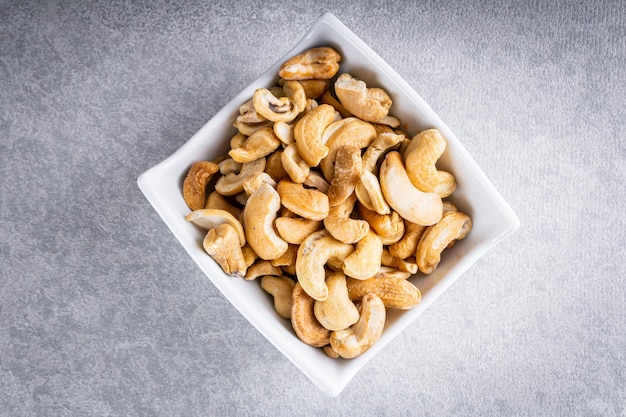 Cashew nuts in crockery pot on white wooden background