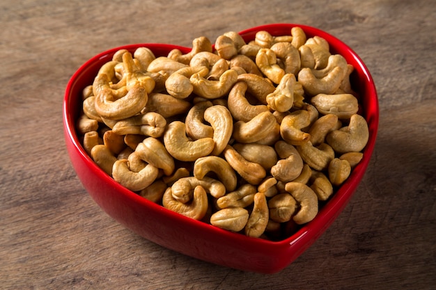 Cashew nuts in heart pot on wood background