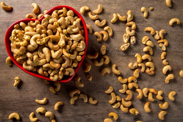 Cashew nuts in heart pot on wood background