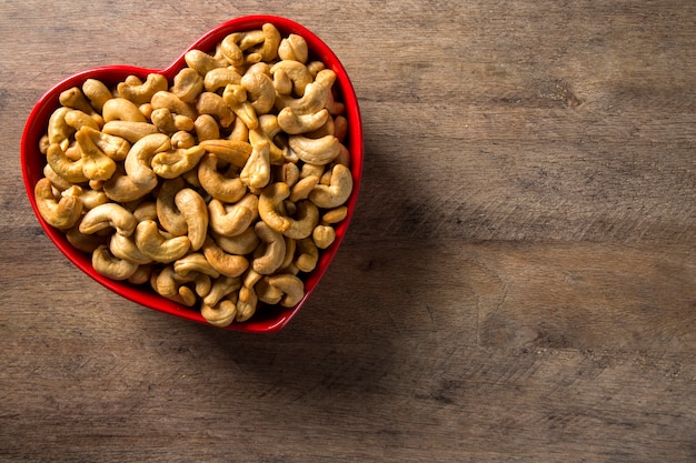 Cashew nuts in heart pot on wood background