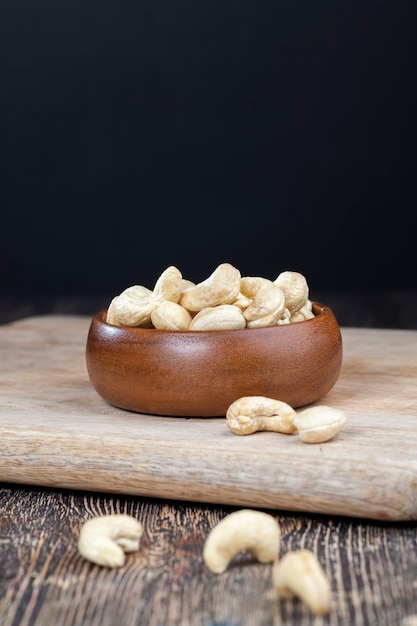 Cashew nuts on an old wooden table and in a wooden bowl, close-up of a large number of cashew nuts on a table and on a wooden surface in a wooden plate