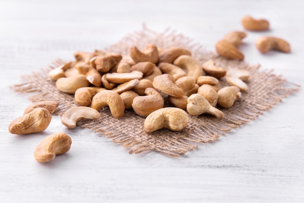 Photo cashew nuts on the piece of burlap on the white wooden table. catalog.