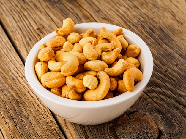 Cashew nuts in  white cup on brown wooden background, side view