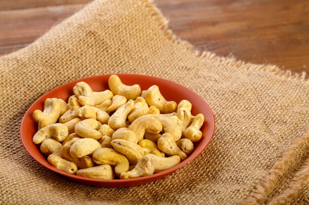 Cashewnoten in een kleiplaat op jute op een houten tafel.