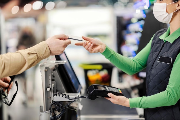 A cashier taking credit card and charging for groceries at supermarket during covid 19