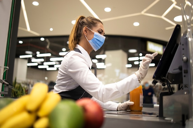 Cashier with protective hygienic mask and gloves working in supermarket and fighting against corona virus pandemic.