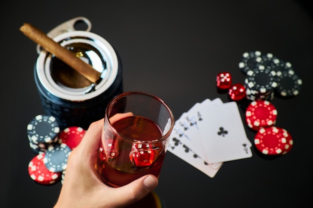Фишки казино, игральные карты, стакан виски и кубики на темном светоотражающем фоне