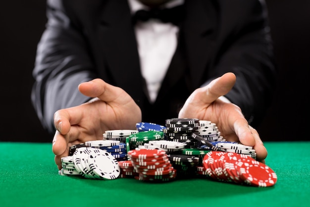 Concetto di casinò, gioco d'azzardo, poker, persone e intrattenimento - primo piano del giocatore di poker con fiches al tavolo del casinò verde