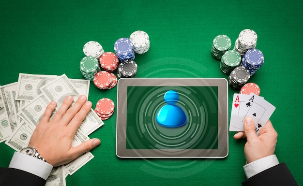 casino, online gokken, technologie en mensenconcept - close-up van pokerspeler met speelkaarten, tablet pc-computer en chips aan groene casinotafel