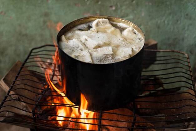 Cassava being cooked in iron pan with wood fire on top of a\
grill