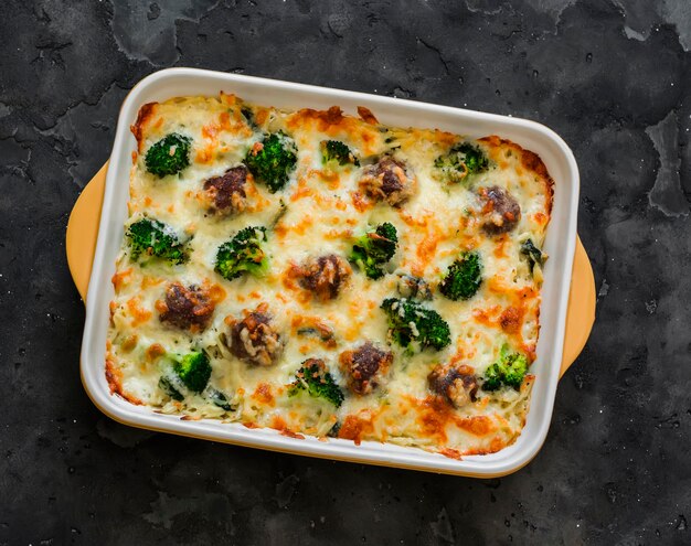 Casserole with meatballs oregano broccoli and cheese in a baking dish on a dark background top view