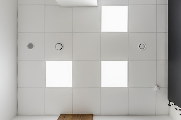 Cassette stretched or suspended ceiling with square halogen\
spots lamps and drywall construction with fire alarm and\
ventilation in empty room in house or office looking up view