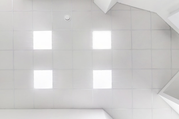 Cassette suspended ceiling with square halogen spots lamps and\
drywall construction in empty room in apartment or house stretch\
ceiling white and complex shape looking up view