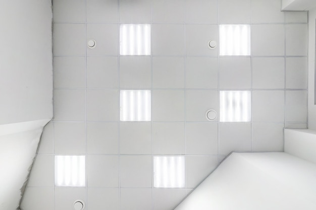 正方形のハロゲンスポットランプとアパートや家の空の部屋の乾式壁構造のカセット吊り天井白くて複雑な形のストレッチ天井ビューを見上げる