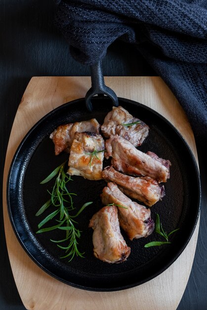 Cast-iron black round pan with fried pork on the black or blue background, top view.