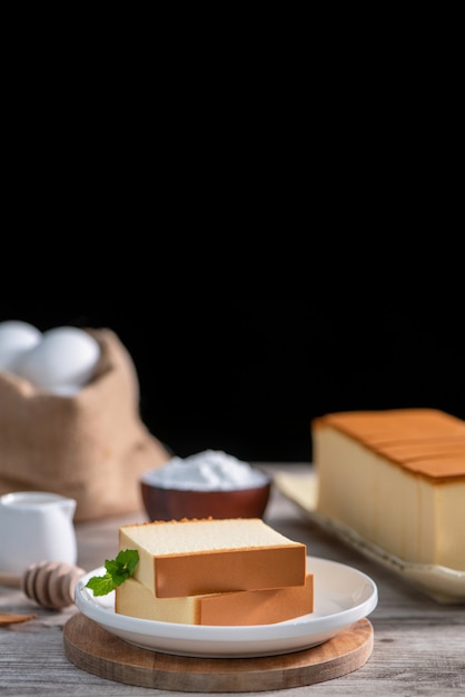 Castella (kasutera) - delizioso cibo giapponese a fette di pan di spagna su piatto bianco su tavola in legno rustico, primo piano, mangiare sano, copia spazio design.