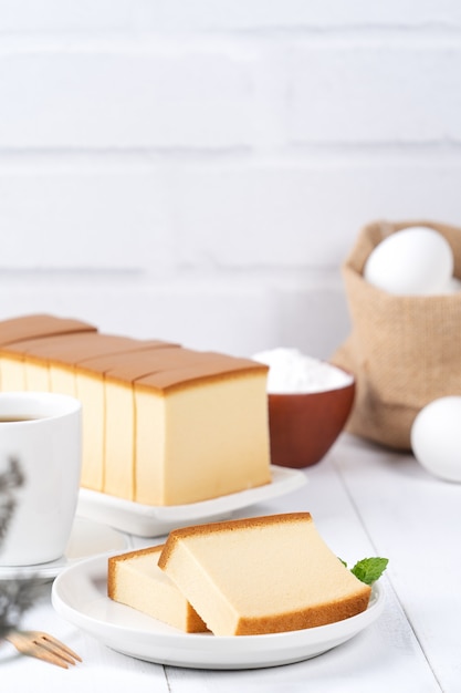 Castella (kasutera) - Mooi heerlijk Japans gesneden biscuitgebakvoedsel op witte plaat over rustieke witte houten lijst, sluit omhoog, exemplaarruimteontwerpconcept.