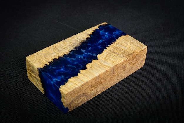 Casting blue epoxy resin with nature burl maple wood cube on black background