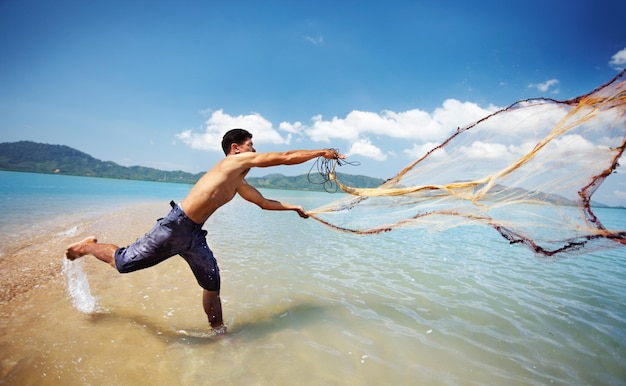 Casting his nets shot of a traditional thai fisherman standing in the water casting a net into the o