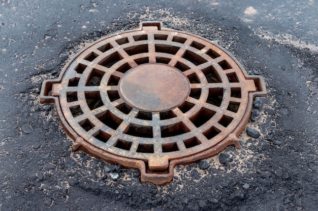 Castiron manhole of the storm sewer system on the road in front of the asphalt pavement