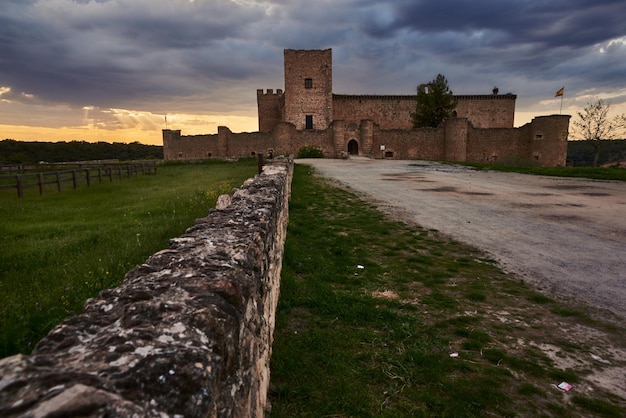 Photo a castle in the countryside with a stone fence and a cloudy sky in pedraza, spain