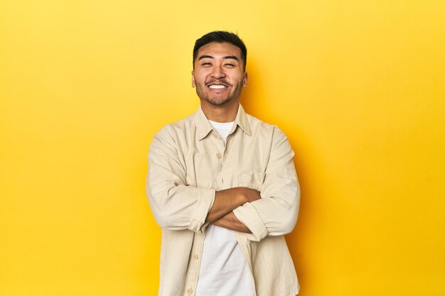 Casual Asian man with open shirt white tee on yellow studio who feels confident crossing arms