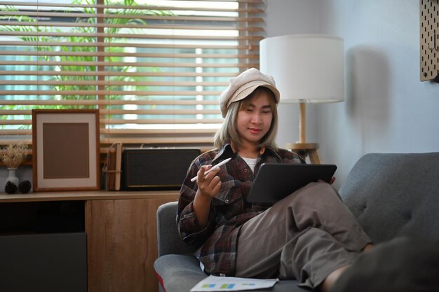 Casual asian woman working with digital tablet while sitting on couch.