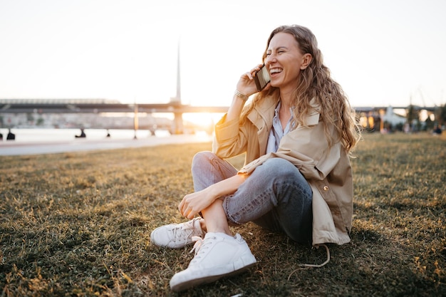 Casual blonde woman sitting on lawn and talking on the phone