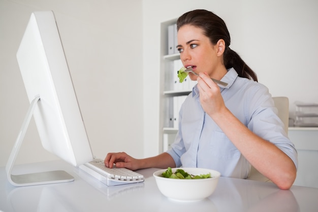 彼女の机でサラダを食べるカジュアルなブルネットの実業家