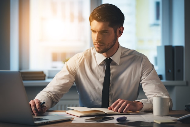 カジュアルな営業日。彼のラップトップを使用して物思いにふける若いハンサムな男