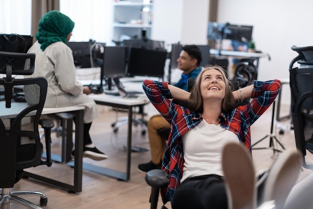 Casual business woman taking a break with legs on her table while working on desktop computer in mod...