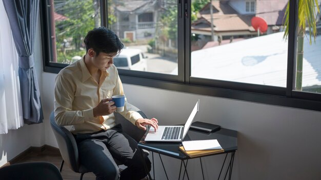 Photo casual businessman drinking coffee and surfing internet on laptop computer at office in the morning.