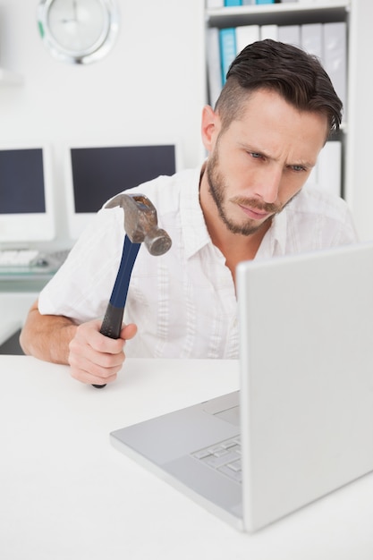 Casual businessman holding hammer over laptop