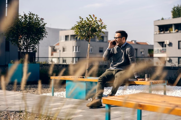 カジュアルなビジネスマンは、都市の外観に座って電話での会話をしています。