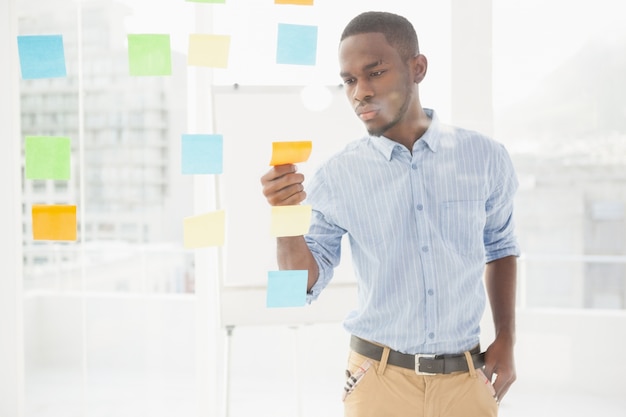 Casual businessman reading sticky notes on window