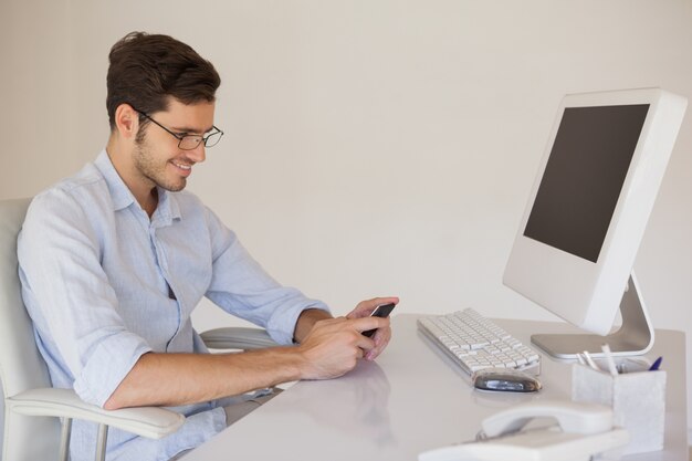 Casual businessman sending a text at his desk